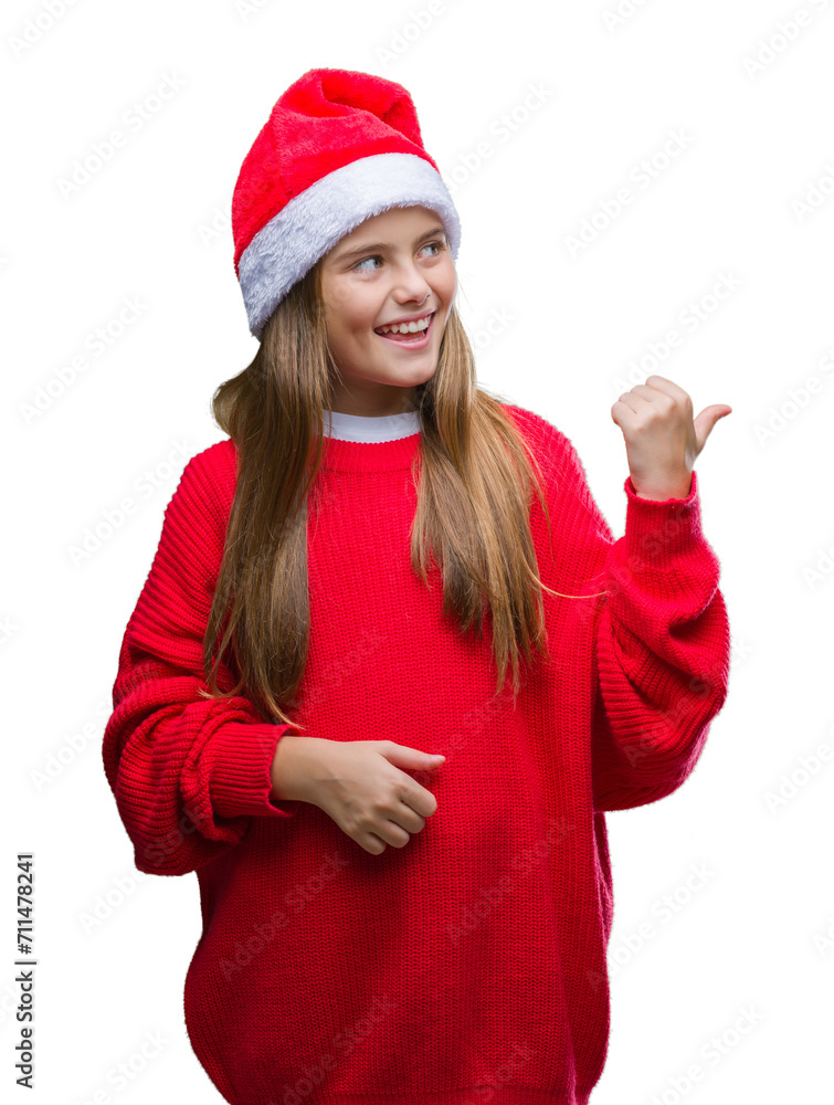 Young beautiful girl wearing christmas hat over isolated background smiling with happy face looking and pointing to the side with thumb up. Young beautiful girl wearing christmas hat over isolated background smiling with happy face looking and pointing to the side with thumb up.