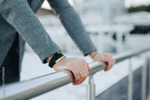 Man in classic suit and bracelet on hand leans on a handrail