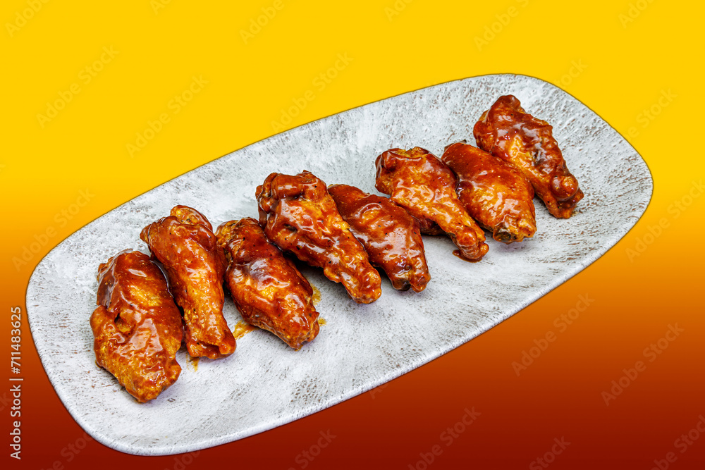 Plate of barbecued chicken wings on a yellow and red gradient background Plate of barbecued chicken wings on a yellow and red gradient background