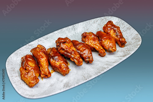 Plate of barbecued chicken wings on a magenta and light blue gradient background