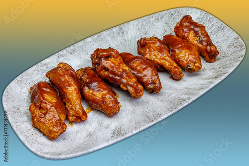 Plate of barbecued chicken wings on a yellow and light blue gradient background