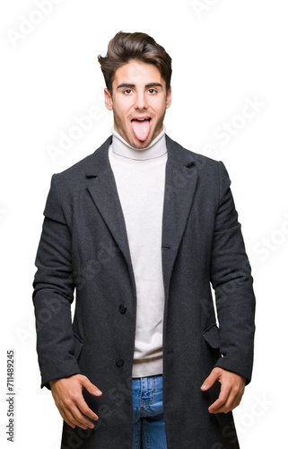 Young elegant man wearing winter coat over isolated background sticking tongue out happy with funny expression. Emotion concept.