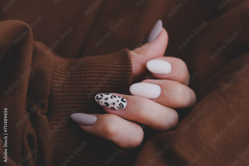 Woman's hand with a beautiful oval-shaped manicure. Autumn trend, beige color polishing with leopard pattern on nails with gel polish, shellac. - obrazy, fototapety, plakaty 