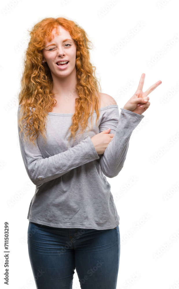 Young redhead woman smiling with happy face winking at the camera doing victory sign. Number two.