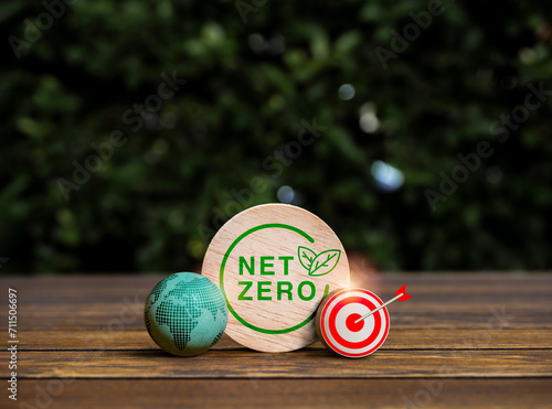 Reduce CO2 emissions, limit climate change, global warming, Net Zero carbon dioxide reduction concept. 3d earth and target icon with Net Zero logo on round wood block on wood table, green background.
