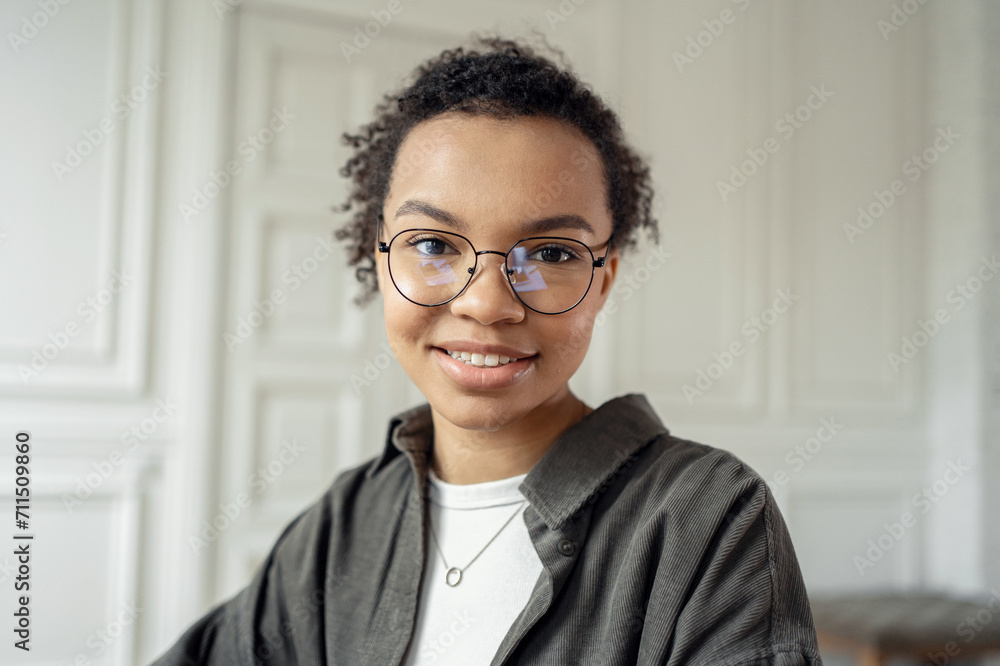 Confident young woman with glasses and curly hair smiling in a well-lit, classic room. Confident young woman with glasses and curly hair smiling in a well-lit, classic room.