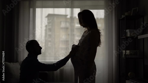 The husband returned after work and hugs the belly of his pregnant wife. Young parents are waiting for the birth of a child. The child pushes in the stomach.