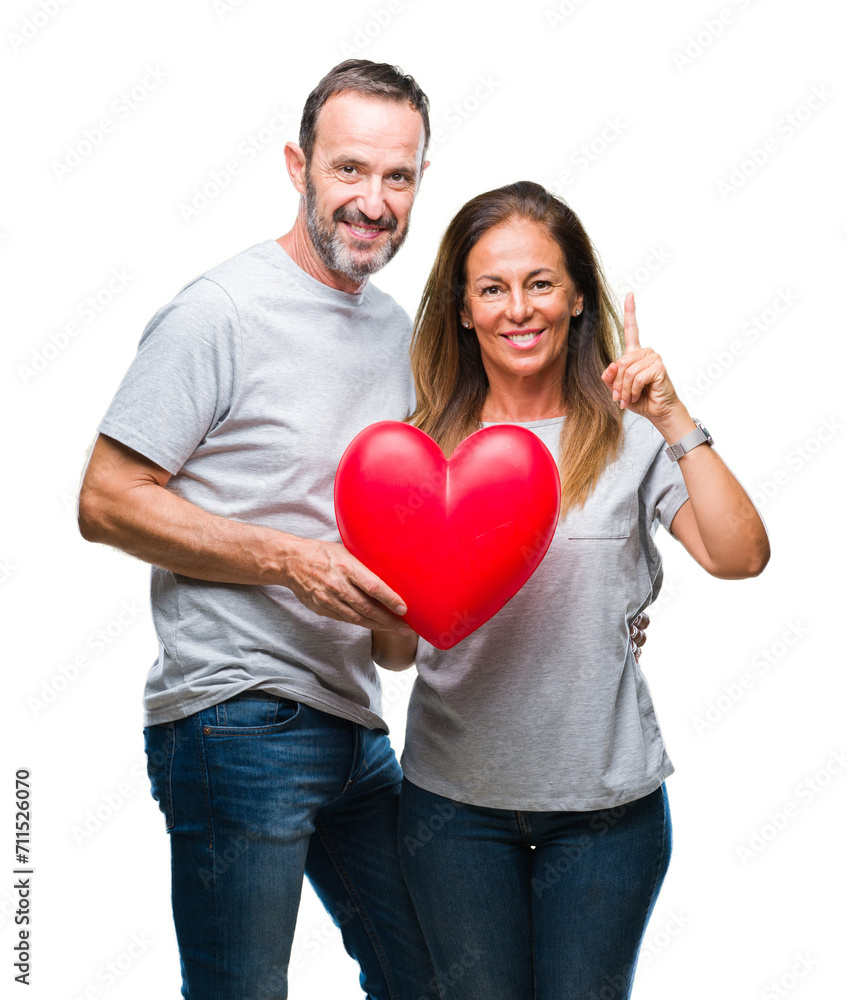 Middle age hispanic casual couple in love holding red heart over isolated background surprised with an idea or question pointing finger with happy face, number one