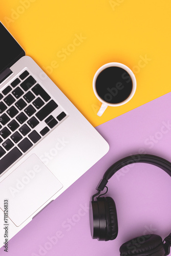 Headphones, cup of black coffee and laptop on a yellow and purple background. Minimal business concept.