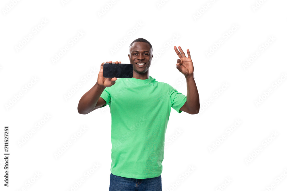 Fototapeta premium young charismatic american man in green t-shirt and jeans showing smartphone screen with mockup