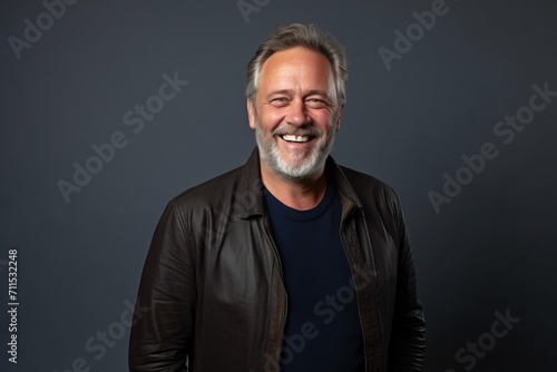 Portrait of a happy senior man in leather jacket smiling against grey background