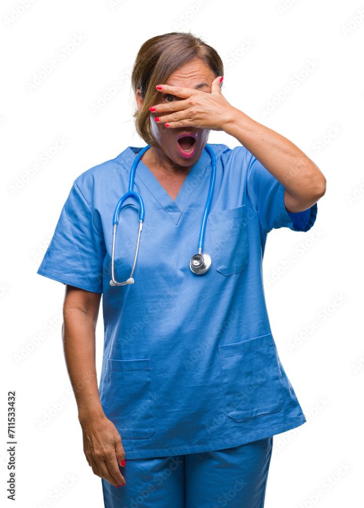 Middle age senior nurse doctor woman over isolated background peeking in shock covering face and eyes with hand, looking through fingers with embarrassed expression. Middle age senior nurse doctor woman over isolated background peeking in shock covering face and eyes with hand, looking through fingers with embarrassed expression.