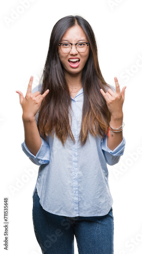 Young asian business woman wearing glasses over isolated background shouting with crazy expression doing rock symbol with hands up. Music star. Heavy concept.