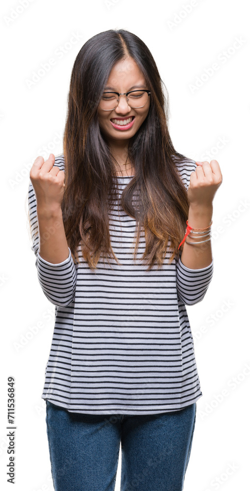 Young asian woman wearing glasses over isolated background very happy and excited doing winner gesture with arms raised, smiling and screaming for success. Celebration concept. Young asian woman wearing glasses over isolated background very happy and excited doing winner gesture with arms raised, smiling and screaming for success. Celebration concept.