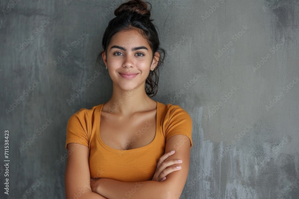 Smiling Latin woman with crossed arms on grey wall.