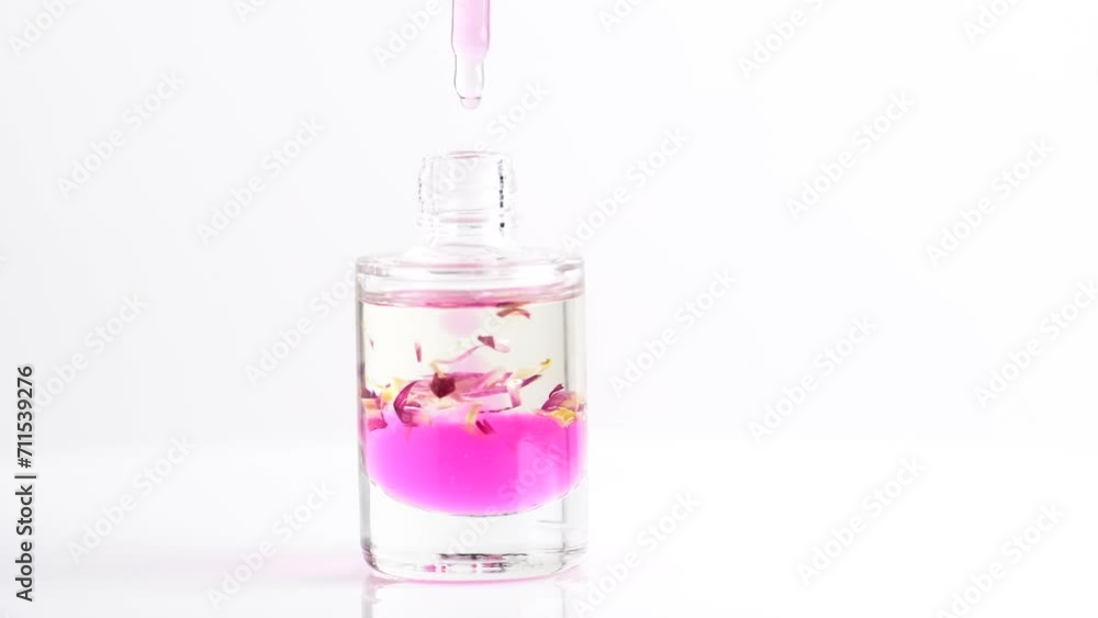 Pipette with cosmetic pink oil for massage and drops flowing into a transparent bottle, close-up. Pipette with cosmetic pink oil for massage and drops flowing into a transparent bottle, close-up.