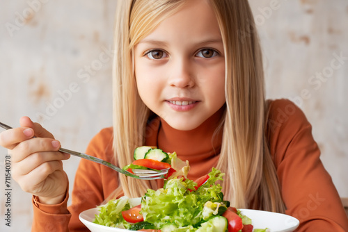 girl eats salad. little beautiful girl with blond long hair sits at the table and eats salad with a fork  healthy food concept