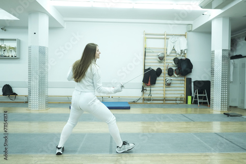 Professional fencer girl with fencing mask and rapier. Training in hall