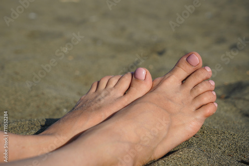 Close-up - female feet on the background of sand on the beach. Woman feet close-up relaxing on beach, enjoying sun © HV