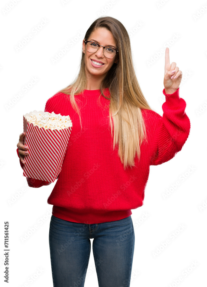Beautiful young woman eating popcorn surprised with an idea or question pointing finger with happy face, number one Beautiful young woman eating popcorn surprised with an idea or question pointing finger with happy face, number one