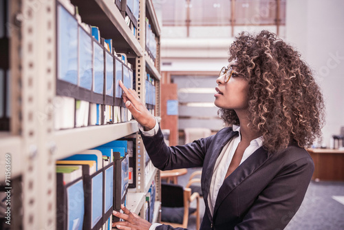 Woman of African descent in business attire looking through binders on library shelf in a large office. Cape Town, South Africa photo