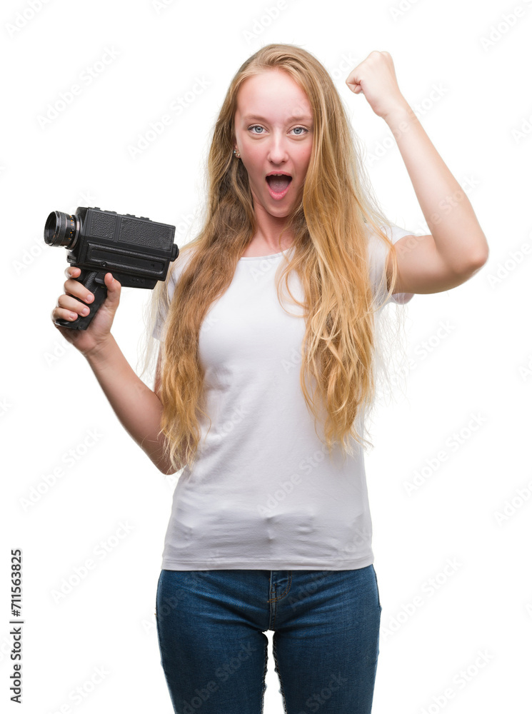 Blonde woman teenager filming holding super 8 video camera annoyed and frustrated shouting with anger, crazy and yelling with raised hand, anger concept Blonde woman teenager filming holding super 8 video camera annoyed and frustrated shouting with anger, crazy and yelling with raised hand, anger concept
