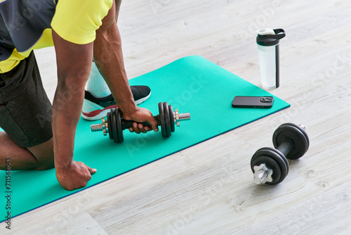 cropped african american man in sportswear working out with dumbbell on fitness mat at home