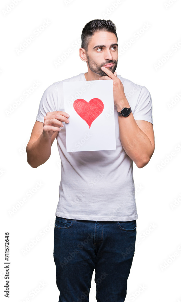 Handsome young man holding card with red heart over isolated background serious face thinking about question, very confused idea Handsome young man holding card with red heart over isolated background serious face thinking about question, very confused idea