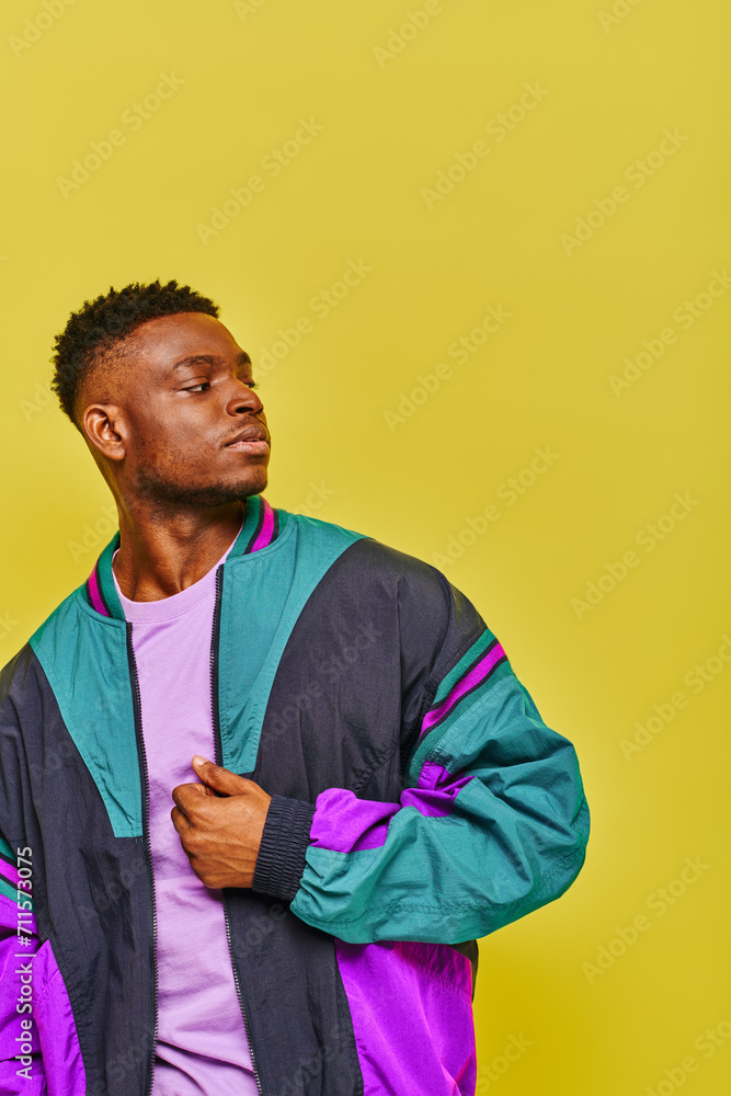 young confident african american man in bright windbreaker looking away on yellow backdrop young confident african american man in bright windbreaker looking away on yellow backdrop