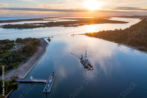 Aerial view over a dredge near a jetty in a coastal river system with a sunset overhead