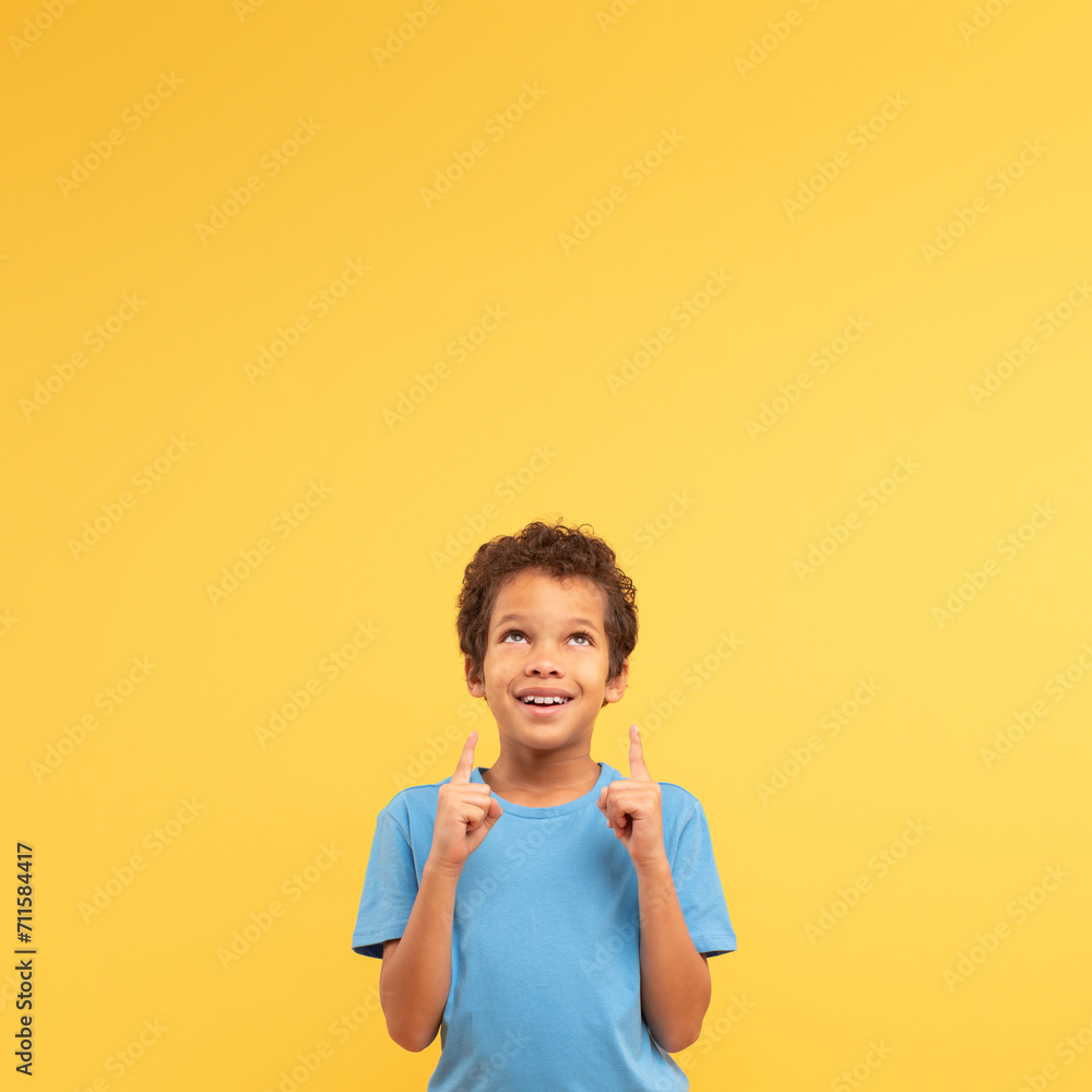 Optimistic boy pointing up, hopeful on yellow square background Optimistic boy pointing up, hopeful on yellow square background