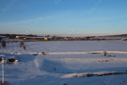 A snowy field with a road and houses in the distance