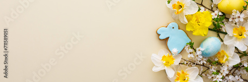 Festive banner with spring flowers and naturally colored eggs and Easter bunnies, white daffodils and cherry blossom branches on a yellow pastel background