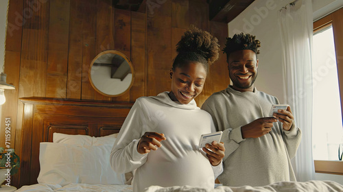 Happy future mixed race parents look positively at pregnancy test, rejoice good news in morning, being young family, pose in cozy bedroom. People, fertility, motherhood and parenthood concept photo