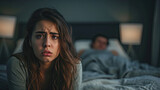 Shot of a woman looking upset while her husband sleeps in the background.