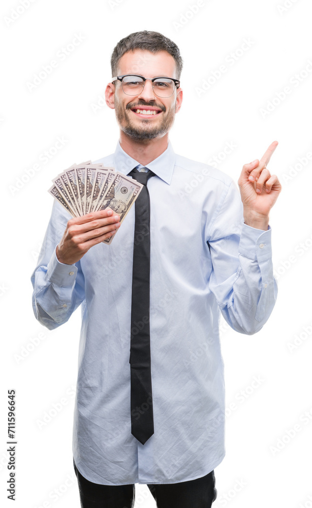 Young hipster business man holding dollars very happy pointing with hand and finger to the side Young hipster business man holding dollars very happy pointing with hand and finger to the side