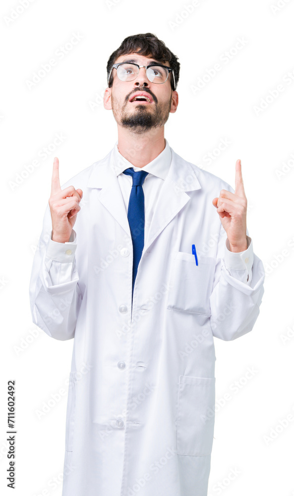 Young professional scientist man wearing white coat over isolated background amazed and surprised looking up and pointing with fingers and raised arms. Young professional scientist man wearing white coat over isolated background amazed and surprised looking up and pointing with fingers and raised arms.