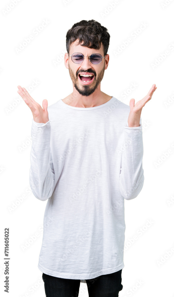 Naklejka premium Young handsome man wearing sunglasses over isolated background celebrating mad and crazy for success with arms raised and closed eyes screaming excited. Winner concept
