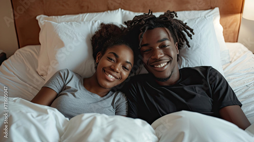 Young calm african loving couple girl guy in t-shirts lying on bed with white sheet pillow blanket indoors in bedroom at home, spending time in room. Rest relax good mood quarantine lifestyle concept