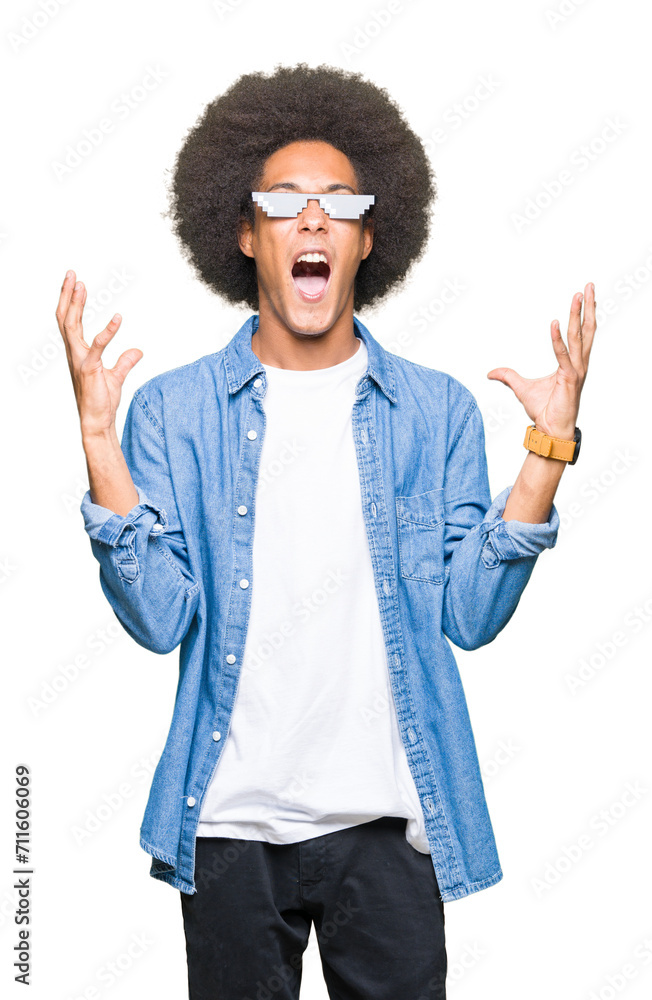 Young african american man with afro hair wearing thug life glasses crazy and mad shouting and yelling with aggressive expression and arms raised. Frustration concept. Young african american man with afro hair wearing thug life glasses crazy and mad shouting and yelling with aggressive expression and arms raised. Frustration concept.