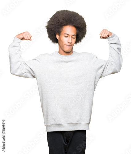 Young african american man with afro hair wearing sporty sweatshirt showing arms muscles smiling proud. Fitness concept.