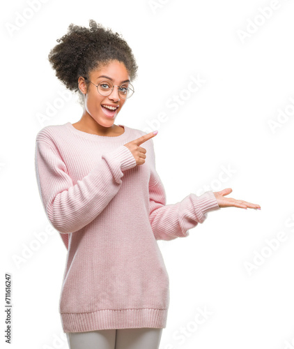 Young afro american woman wearing glasses over isolated background amazed and smiling to the camera while presenting with hand and pointing with finger.
