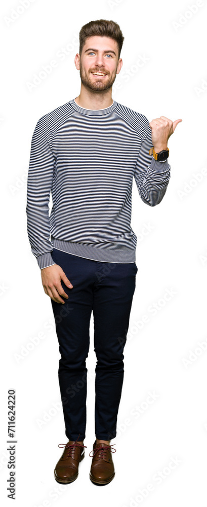 Young handsome man wearing stripes sweater smiling with happy face looking and pointing to the side with thumb up. Young handsome man wearing stripes sweater smiling with happy face looking and pointing to the side with thumb up.