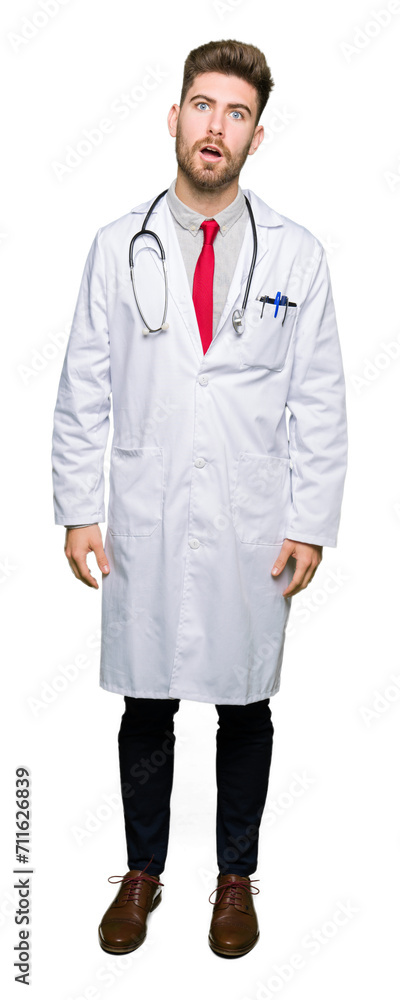 Young handsome doctor man wearing medical coat In shock face, looking skeptical and sarcastic, surprised with open mouth Young handsome doctor man wearing medical coat In shock face, looking skeptical and sarcastic, surprised with open mouth