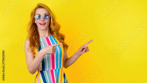 Woman and pointing at mockup workspace for advert, marketing, promotion or text. Fashionable redhead lady showing mock up for advertising, news deal of offer, trendy makeup, outfit, yellow background