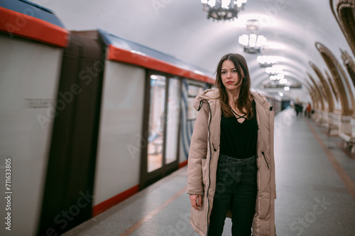 A young woman stands on the platform at the metro station, a train arrives.