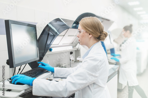 A laboratory technician in a lab coat performs a series of tests on a chemical analyzer in a bio laboratory. impersonal unrecognizable laboratory blurred fuzzy background shot through glass with space
