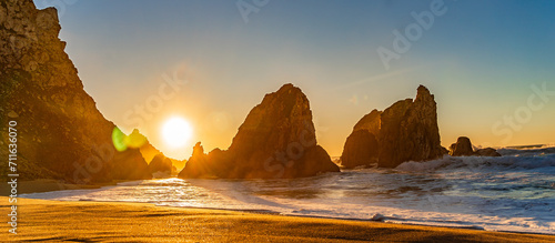 Sunset on the Portugal Ursa Beach, Praia da Ursa, the westernmost beach at atlantic coast of Atlantic Ocean with sand and sunset sun waves and foam at sand of coastline picturesque landscape panorama