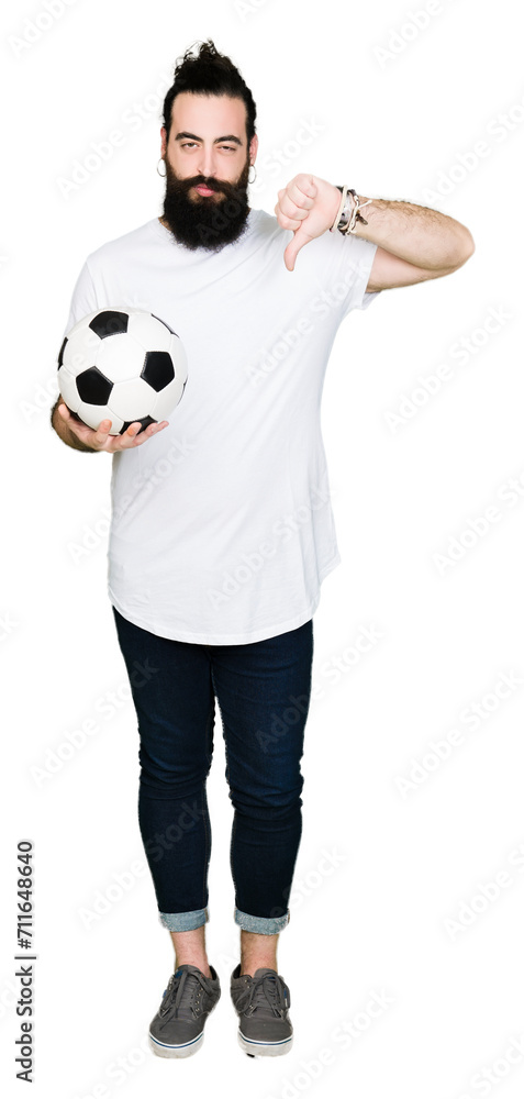 Young man with long hair and bear holding soccer football ball with angry face, negative sign showing dislike with thumbs down, rejection concept