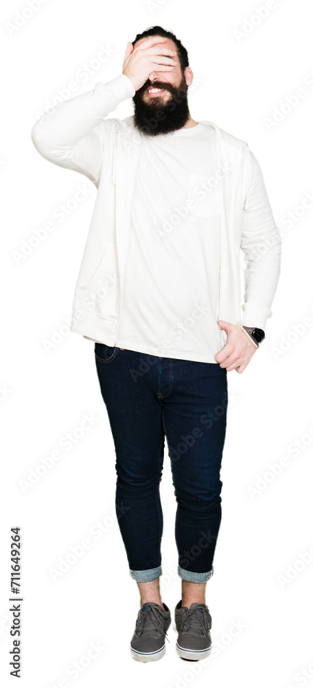 Young man with long hair and beard wearing sporty sweatshirt smiling and laughing with hand on face covering eyes for surprise. Blind concept. Young man with long hair and beard wearing sporty sweatshirt smiling and laughing with hand on face covering eyes for surprise. Blind concept.